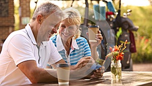 Senior Couple Sitting Having Coffee After Round Of Golf Looking At Score Card Together