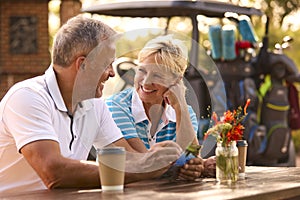 Senior Couple Sitting Having Coffee After Round Of Golf Looking At Score Card Together