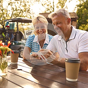 Senior Couple Sitting Having Coffee After Round Of Golf Looking At Score Card Together