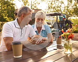 Senior Couple Sitting Having Coffee After Round Of Golf Looking At Score Card Together