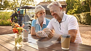 Senior Couple Sitting Having Coffee After Round Of Golf Looking At Score Card Together