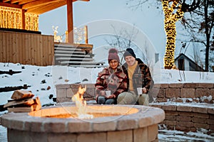 Senior couple sitting and heating together at outdoor fireplace in winter evening.