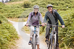 Senior couple sitting on mountain bikes in a country lane during a camping holiday, looking at camera, front view