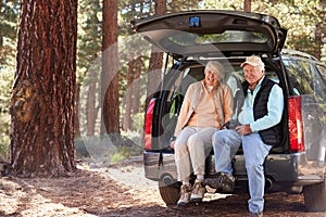 Senior couple sitting in open car trunk preparing for a hike