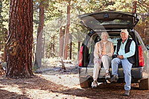 Senior couple sitting in open car trunk preparing for a hike