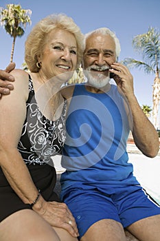 Senior Couple sitting outdoors man using mobile phone portrait.