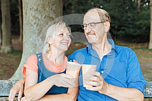 Senior couple sitting on a park bench, relaxing and drinking coffee to go from bamboo reusable cups