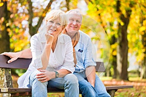 Senior couple sitting on part bench in fall