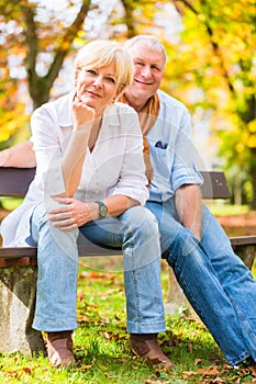 Senior couple sitting on part bench in fall
