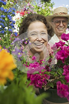 Senior Couple sitting in plant nursery seen through bed of flowers portrait