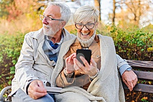 Senior couple sitting in public park using smart device to shop online