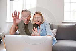 Senior Couple Sitting On Sofa At Home Making Video Call Using Laptop Computer Together