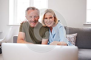 Senior Couple Sitting On Sofa At Home Making Video Call Using Laptop Computer Together