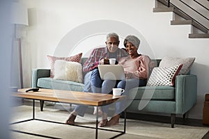 Senior Couple Sitting On Sofa At Home Using Laptop To Shop Online