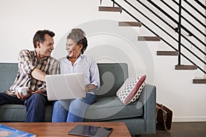 Senior Couple Sitting On Sofa At Home Using Laptop Together