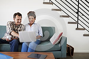 Senior Couple Sitting On Sofa At Home Using Laptop Together