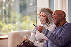 Senior Couple Sitting On Sofa At Home Watching TV Together