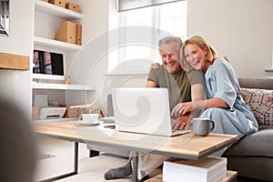 Senior Couple Sitting On Sofa In Lounge At Home Using Laptop Together