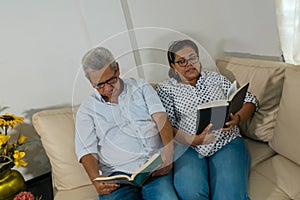 Senior couple sitting on sofa and reading a book in living room