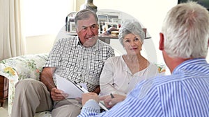 Senior Couple Sitting On Sofa Talking To Financial Advisor