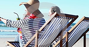 Senior couple sitting on sunlounger and having cocktail at beach