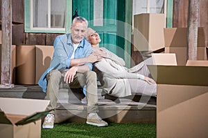 Senior couple sitting together on stairs of new house, relocation concept