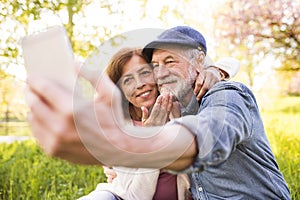 Senior couple with smartphone outside in spring nature.