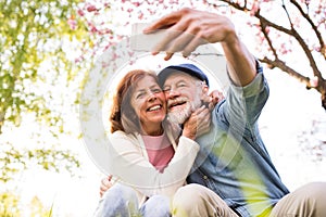 Senior couple with smartphone outside in spring nature.