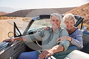 Senior couple smile to camera from open top car, close up