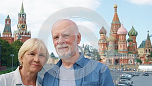 Senior couple stand on background of St. Basil`s Cathedral and Kremlin clock tower in Moscow, Russia