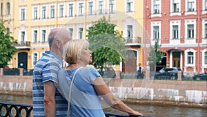 Senior couple stand on quay of canal look around. Pensioners travel in Saint Petersburg, Russia