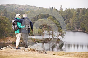 Senior couple standing embracing and admiring the view of a lake, back view