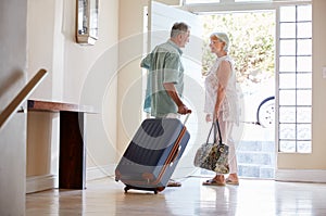Senior Couple Standing By Front Door With Suitcase About To Leave For Vacation