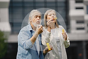 Senior couple standing on a grass in summer and blowing soap bubbles