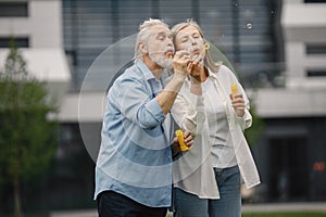 Senior couple standing on a grass in summer and blowing soap bubbles