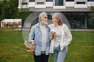 Senior couple standing on a grass in summer with straw basket and flowers