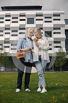 Senior couple standing on a grass in summer with straw basket and flowers