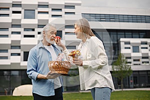 Senior couple standing on a grass in summer with straw basket and flowers