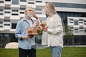 Senior couple standing on a grass in summer with straw basket and flowers