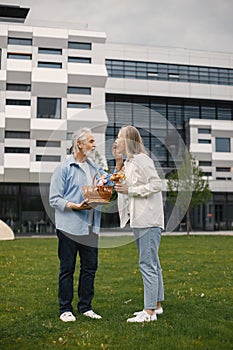 Senior couple standing on a grass in summer with straw basket and flowers