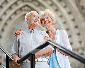 Senior couple standing near iron railings in front of cathedral