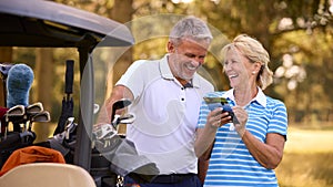 Senior Couple Standing Next To Buggy On Golf Course Marking Score Card Together