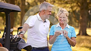 Senior Couple Standing Next To Buggy On Golf Course Marking Score Card Together