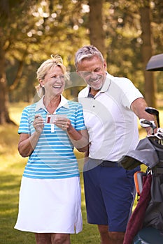 Senior Couple Standing Next To Buggy On Golf Course Marking Score Card Together