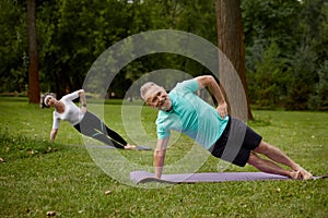 Senior couple standing on side plank exercising for wellbeing outdoors