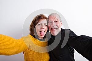 Senior couple sticking tongues out, taking selfie. Studio shot.