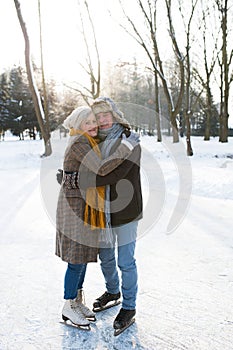 Senior couple in sunny winter nature ice skating, hugging.
