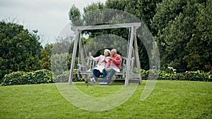 Senior couple on swing in garden with love, conversation and bonding with trees, grass and care. Relax, old man and