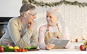 Senior Couple With Tablet Computer Preparing Christmas Dinner In Kitchen