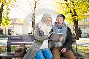 Senior couple with tablet sitting on bench. Autumn park.